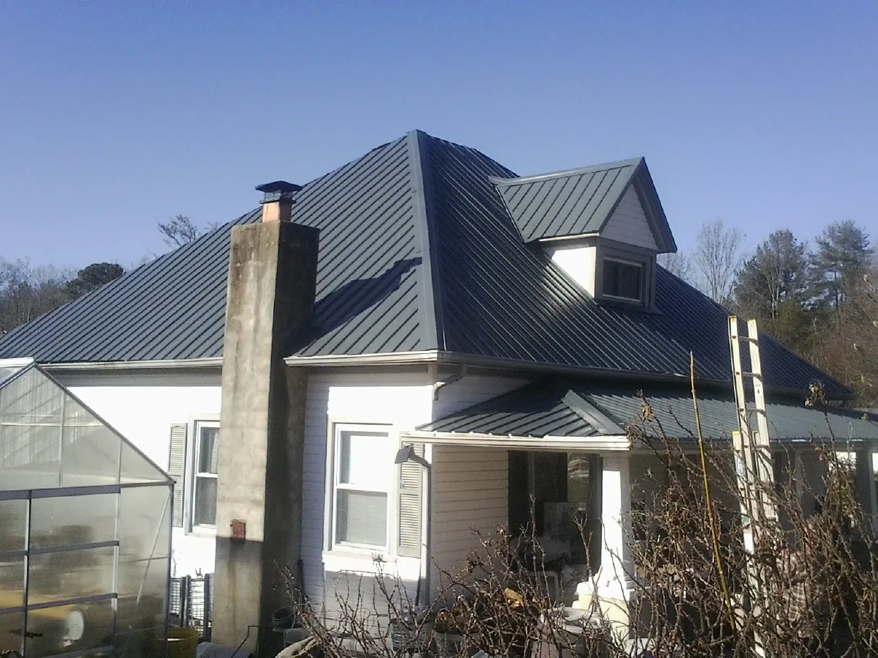 Dark blue standing seam metal roof on a white farmhouse with dormer — Slate & Tile Roof Repair by Roofing Brothers in Day