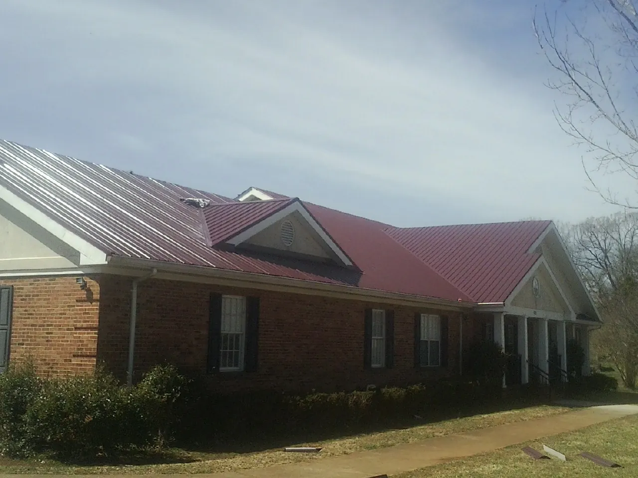Red metal roof with gabled entries on a long brick building, from a Hail Damage Roof Repair job in Day