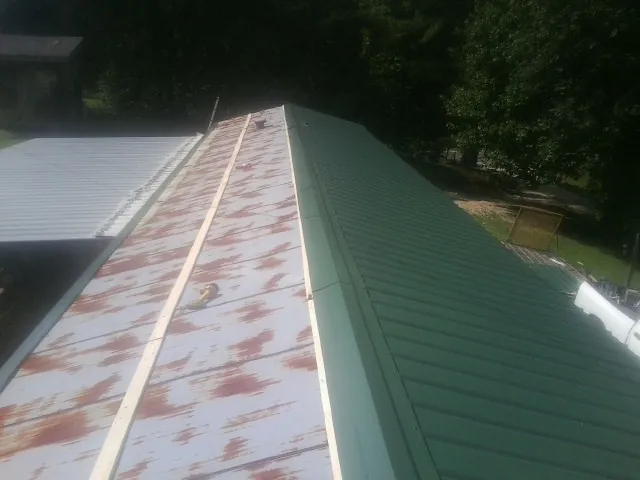 Old rusted panels beside newly installed green metal roofing — Wind Damage Roof Repair by Roofing Brothers in Day