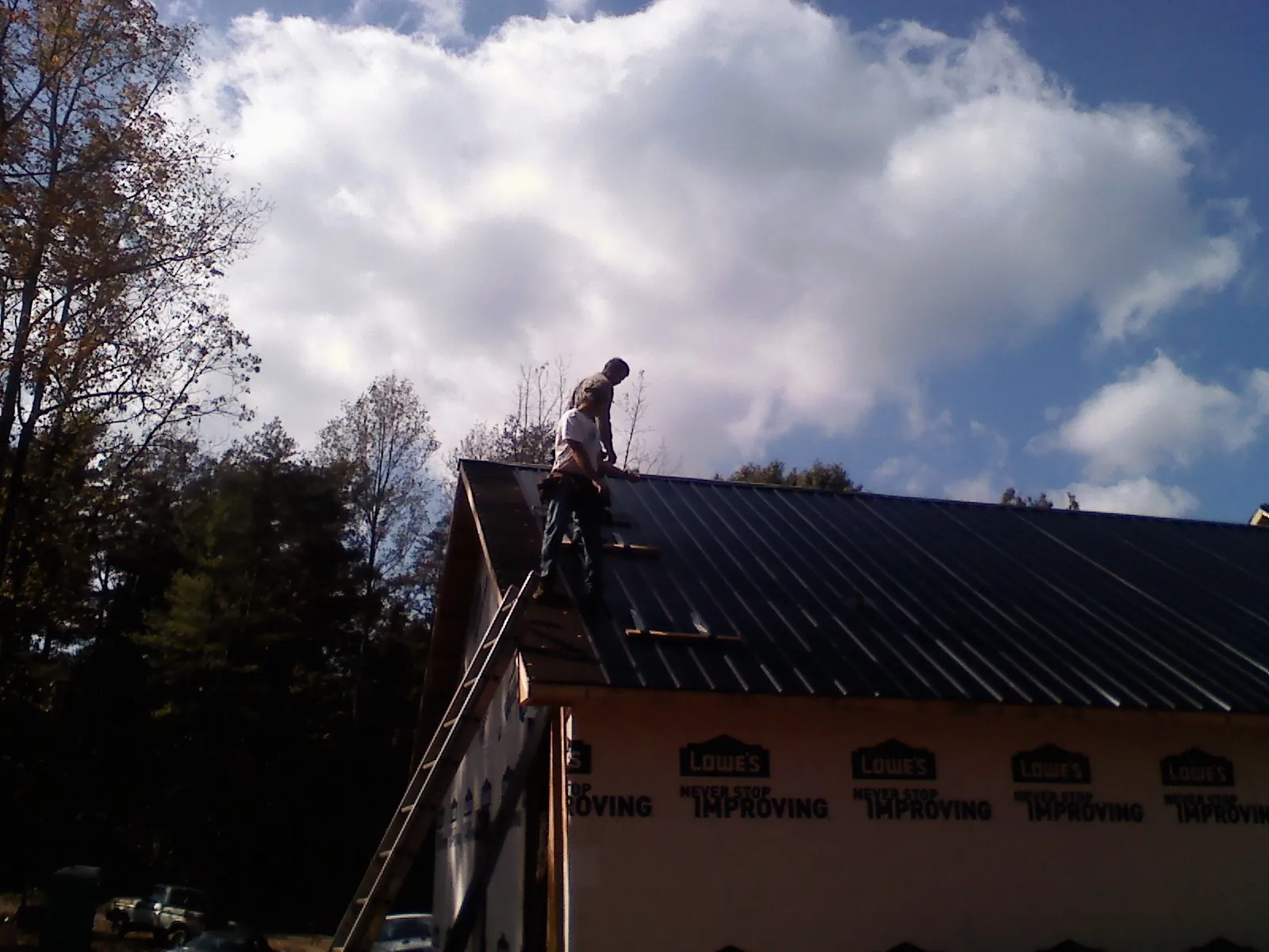 Roofer fastening dark metal panels high against a cloudy sky, from a Roof Inspection job in Day