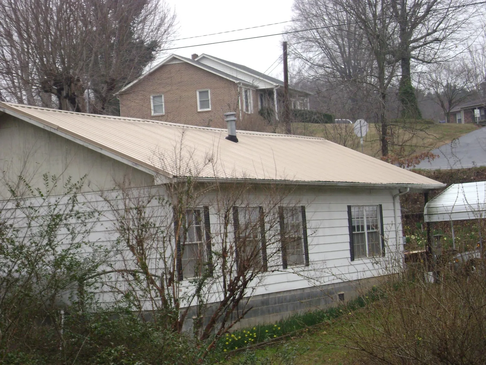 Tan metal roof on a white sided house set into a hillside — Commercial Roofing by Roofing Brothers in Day